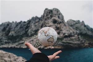 Hand releasing globe toward sea and cliff 