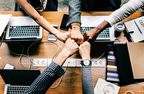 Five hands fist bumping over 3 laptops 