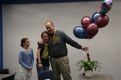 John holding balloons embracing a student