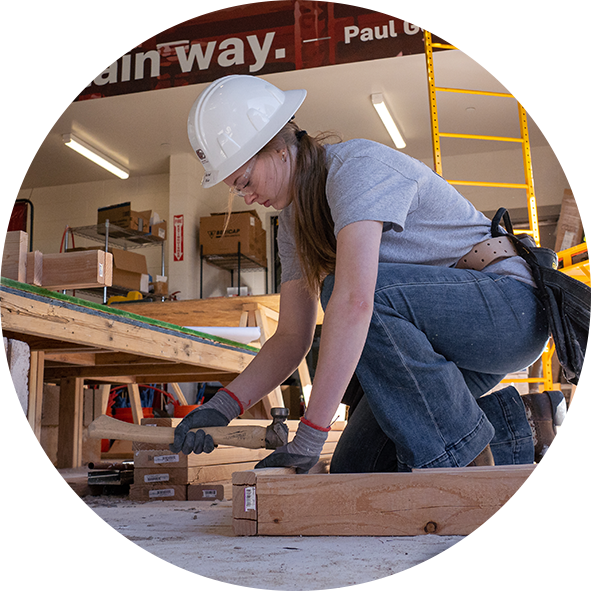 student wearing hard hat working with wood and hammer