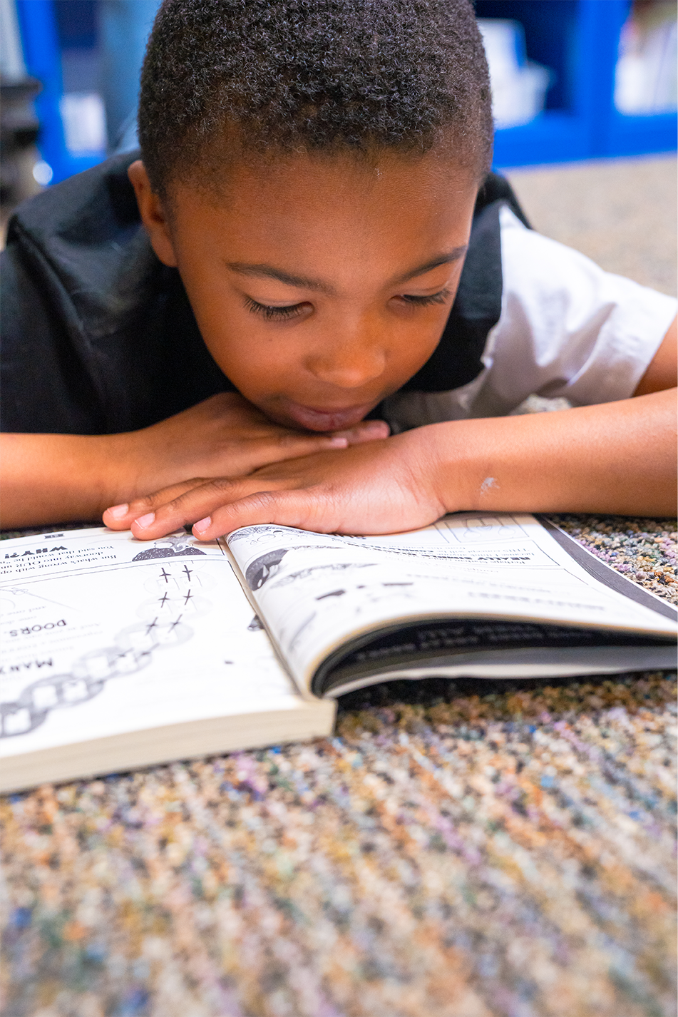 Young student reading book on classroom floor